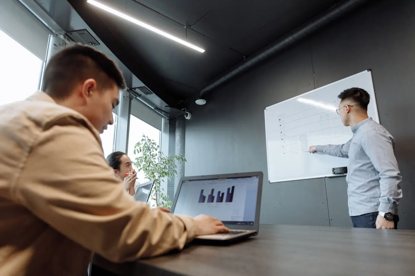 Two colleagues in a meeting room, one writing on a whiteboard